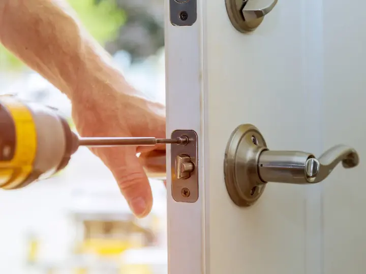 Main tenant répare une serrure cassée sur une porte fermée. Un tournevis est utilisé pour fixer le mécanisme.