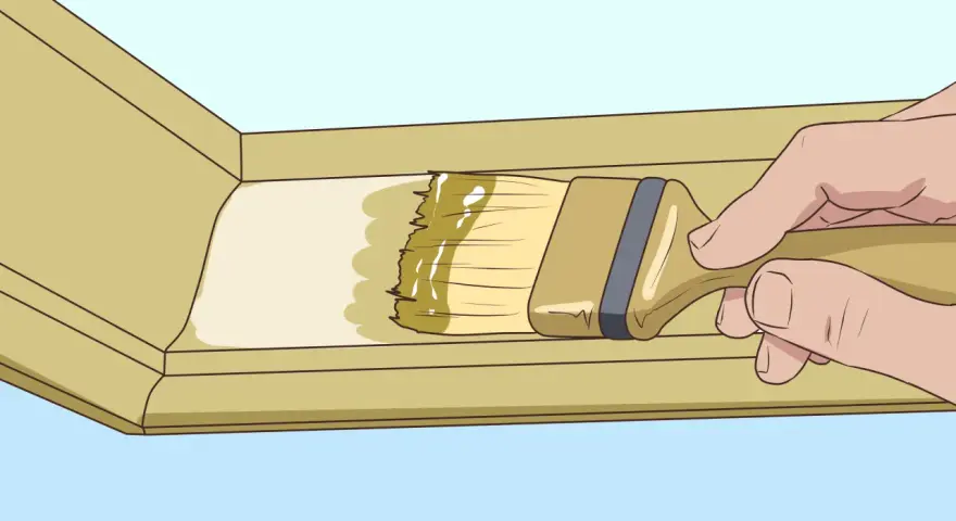 Main tenant pose du mastic sur une moulure en bois avec un pinceau.