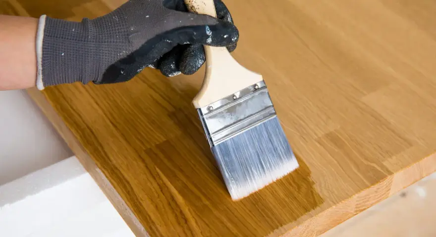 Main tenant enlever huile de lin sur bois avec un pinceau. Le bois est clair et le pinceau applique une couche protectrice.