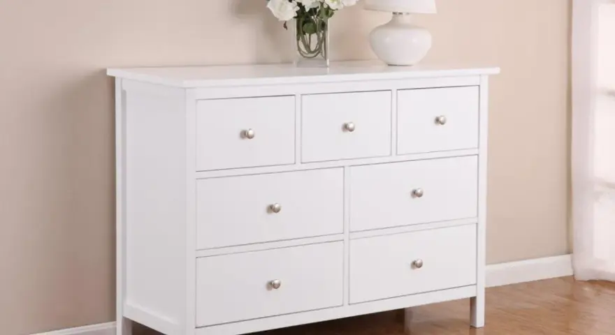 Commode blanche 3 tiroirs, prête à être relookée. Un vase de fleurs et une lampe complètent la scène.