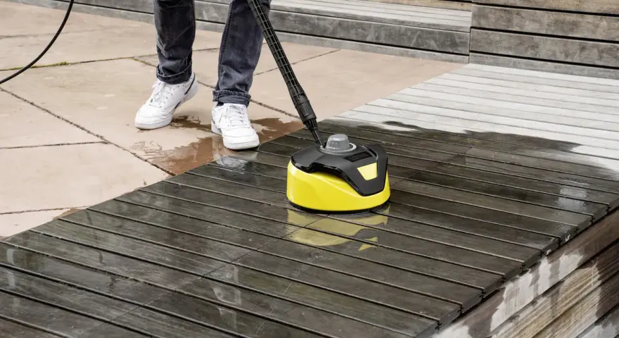 Nettoyage d'une terrasse en bois avec un karcher. L'appareil jaune et noir nettoie le bois sombre, laissant une surface plus claire et humide.