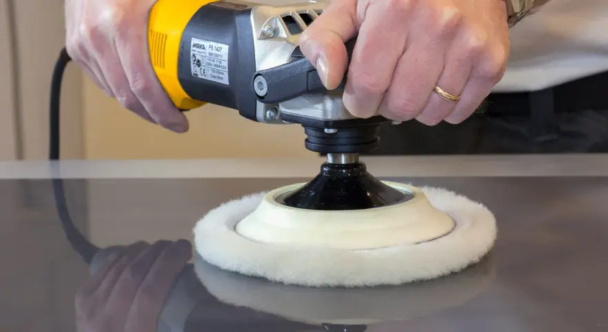 Main d'artisan utilisant une polisseuse pour polir le vernis d'un meuble en bois.