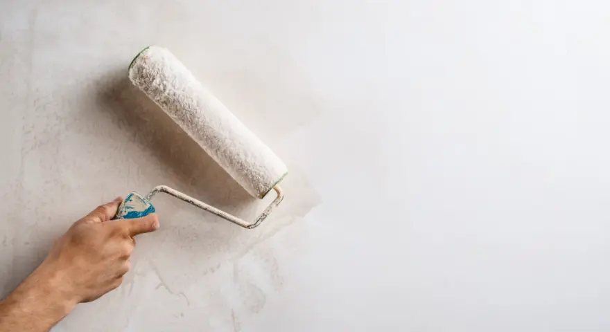 Main d'une personne appliquant une couche de peinture sur un mur déjà peint avec un rouleau.