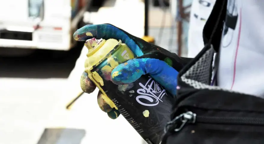 Main tenant une bombe de peinture jaune, un gant coloré montre comment enlever de la bombe de peinture.