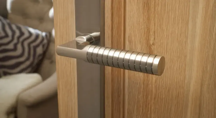 Composition d'une poignée de porte moderne en métal brossé sur une porte en bois clair. Le manche est strié pour une meilleure prise.