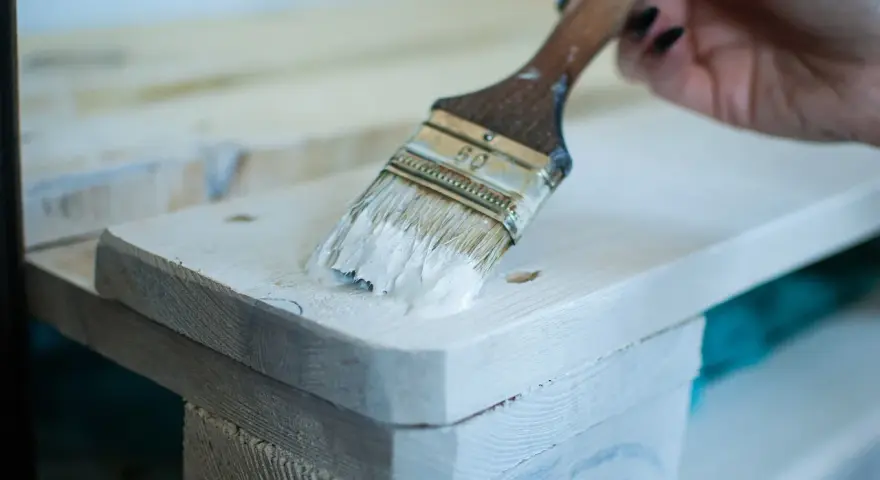Application de peinture glycéro sur bois brut, sans poncer. La brosse dépose une couche blanche sur la surface.