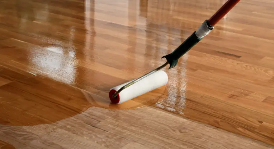 Application d'un vernis ou vitrificateur sur un parquet en bois. Le rouleau dépose une couche brillante et protectrice.