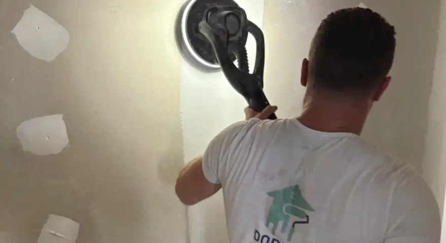 Un ouvrier utilise une ponceuse girafe pour poncer un mur en plâtre, préparant la surface pour la peinture.