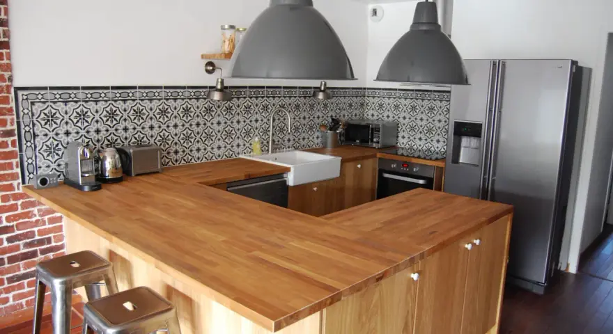 Cuisine moderne avec îlot central en bois, carrelage mural graphique et tabourets industriels. On dirait qu'on a réussi à faire une cuisine avec des vieux meubles revisités.