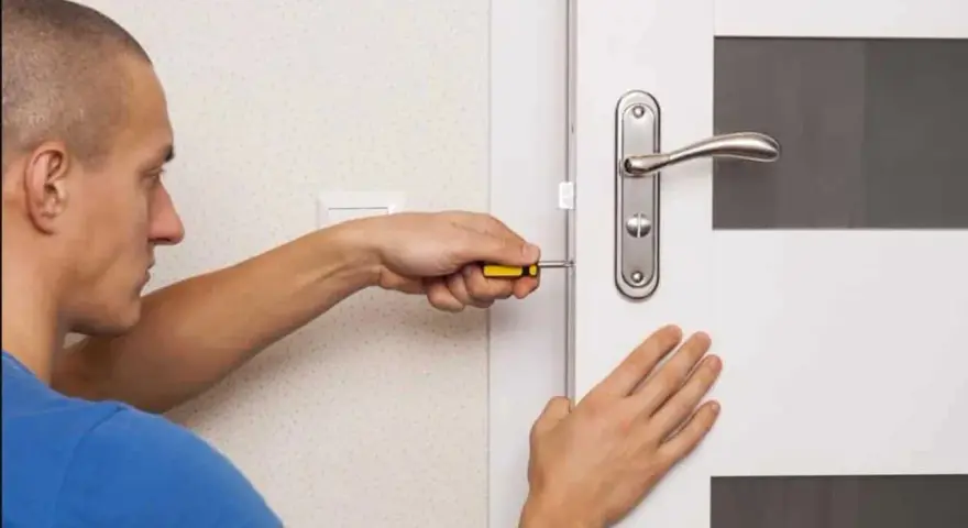 Un homme utilise un tournevis pour installer une serrure sur une porte de chambre.