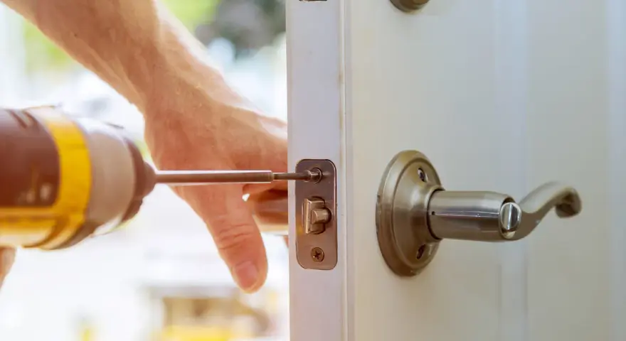 Main tenant répare une serrure cassée sur une porte fermée. Un tournevis est utilisé pour fixer le mécanisme.