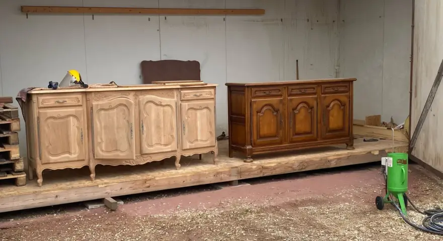 Deux commodes en bois, l'une brute et l'autre vernie, témoignent d'une **réparation meuble en bois**. Un équipement de sablage est prêt à l'emploi.