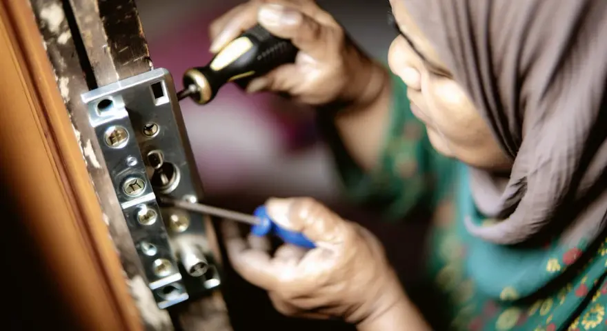 Une personne en hijab utilise un tournevis pour enlever vieux gonds d'une porte en bois.