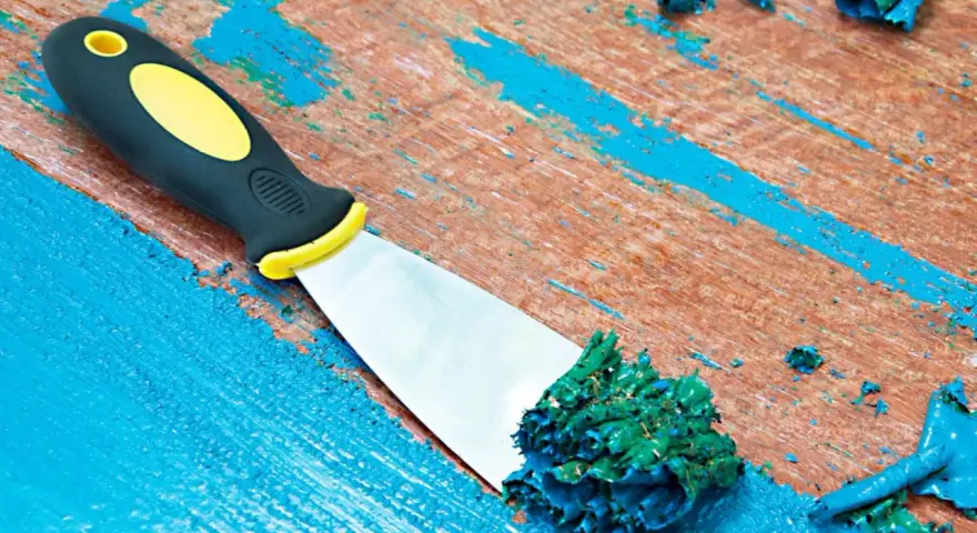 Spatule raclant de la peinture acrylique verte sur une surface en bois bleue écaillée.