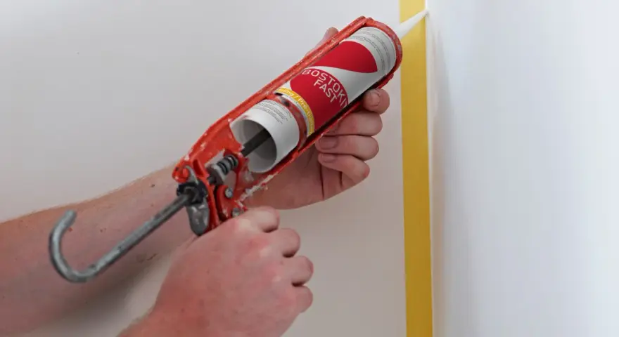 Application de silicone avec un pistolet pour une finition parfaite. Le joint de silicone est appliqué le long d'un coin de mur masqué par du ruban de peintre.
