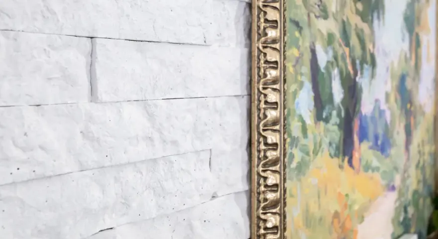 Un mur en pierre peint en blanc sert de toile de fond à un tableau aux couleurs vives, encadré d'or.