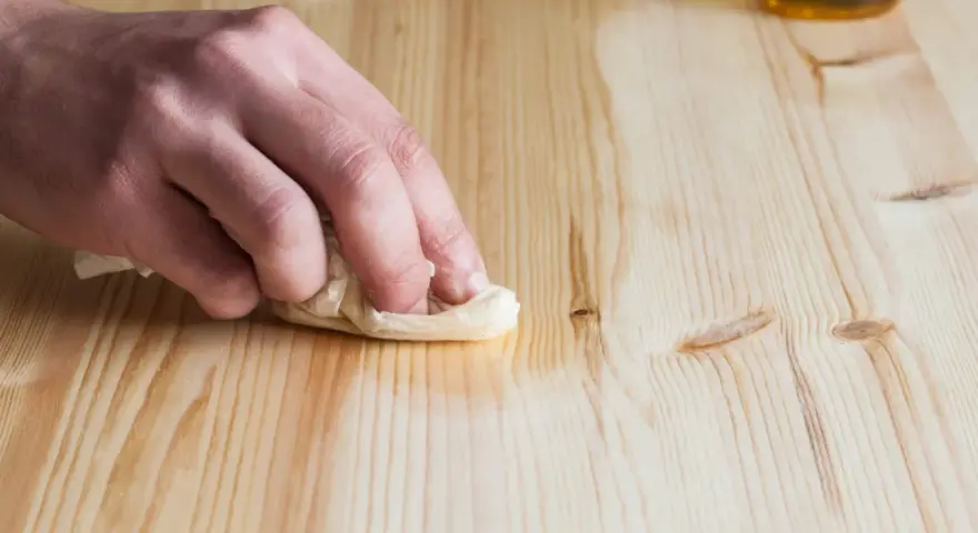 Main d'artisan essuyant un bois fraîchement poncé avec un chiffon humide pour le nettoyer.