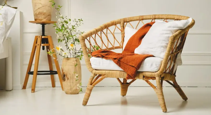 Un fauteuil en rotin tressé, invitant à la détente. Un plaid orange et un coussin blanc ajoutent une touche de confort. L'entretien rotin est essentiel pour préserver sa beauté naturelle.