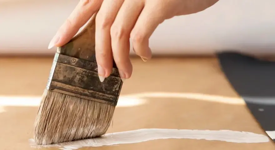 Main d'une personne appliquant une couche de primaire sur du mdf avec un pinceau.