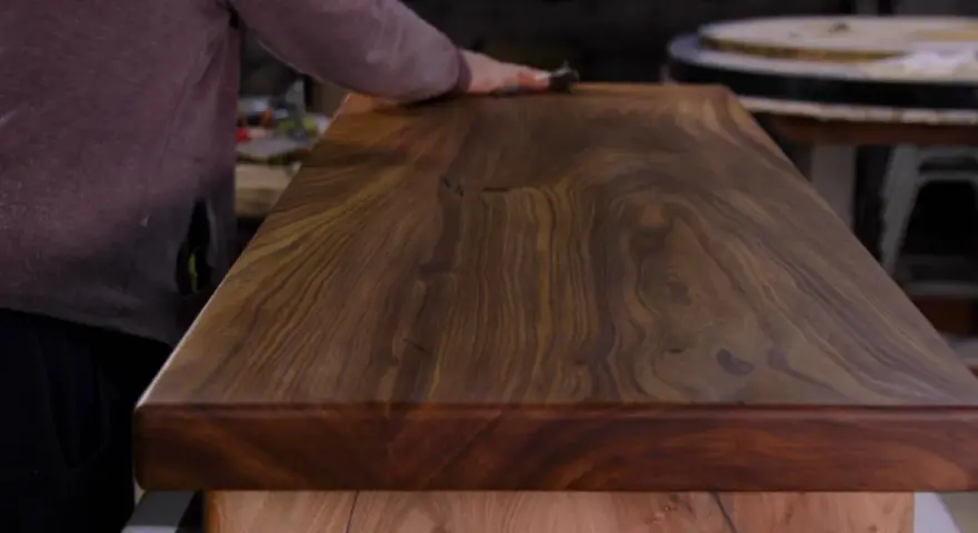 Un artisan polit un meuble en bois de noyer, révélant la beauté du grain. L'essence de térébenthine est utilisée pour faire ressortir la richesse du bois.