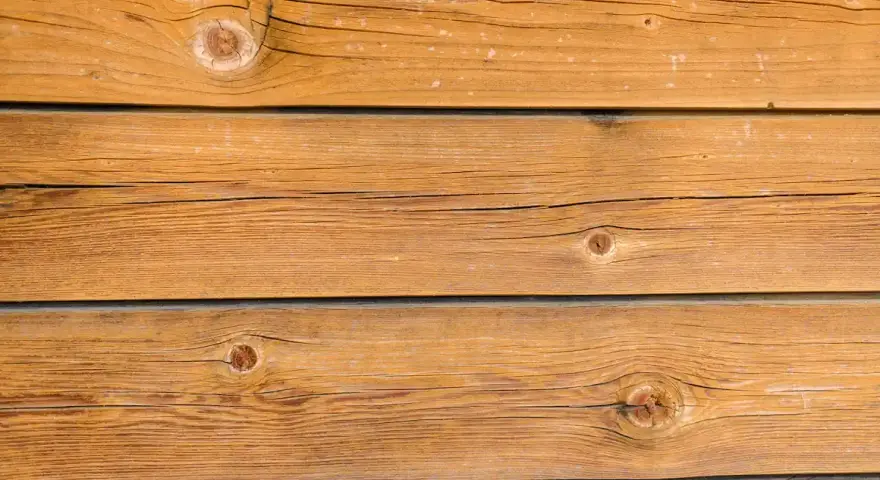Planches de bois brun clair, traitées avec une lasure bois autoclave, révélant des nœuds et des veines naturelles.