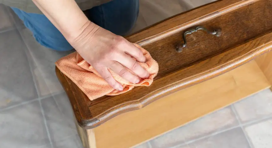 Maintenant, je sais comment nettoyer un meuble avant de le peindre. Une main passe un chiffon orange sur un tiroir en bois verni.