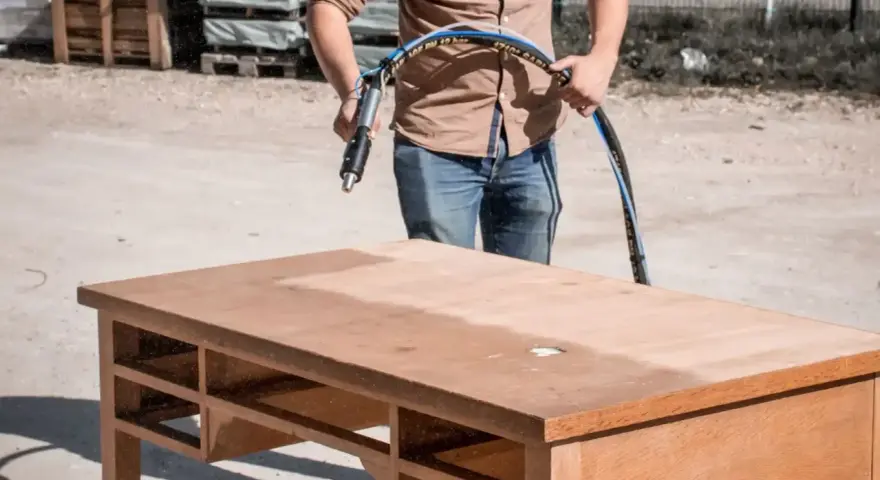 Un homme utilise un appareil pour le décapage chimique bois d'un bureau. La moitié de la surface est déjà propre.