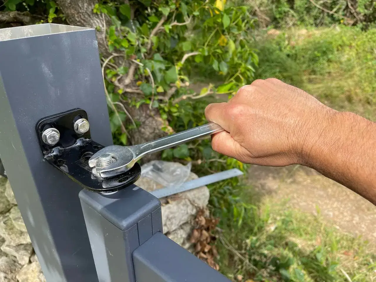 Ajustement du gond d'un portail en aluminium avec une clé.