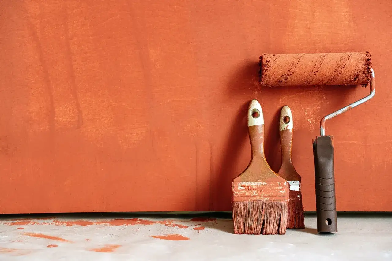 Pinceaux et rouleau à peinture sur fond orange, laissant des traces peinture mur.