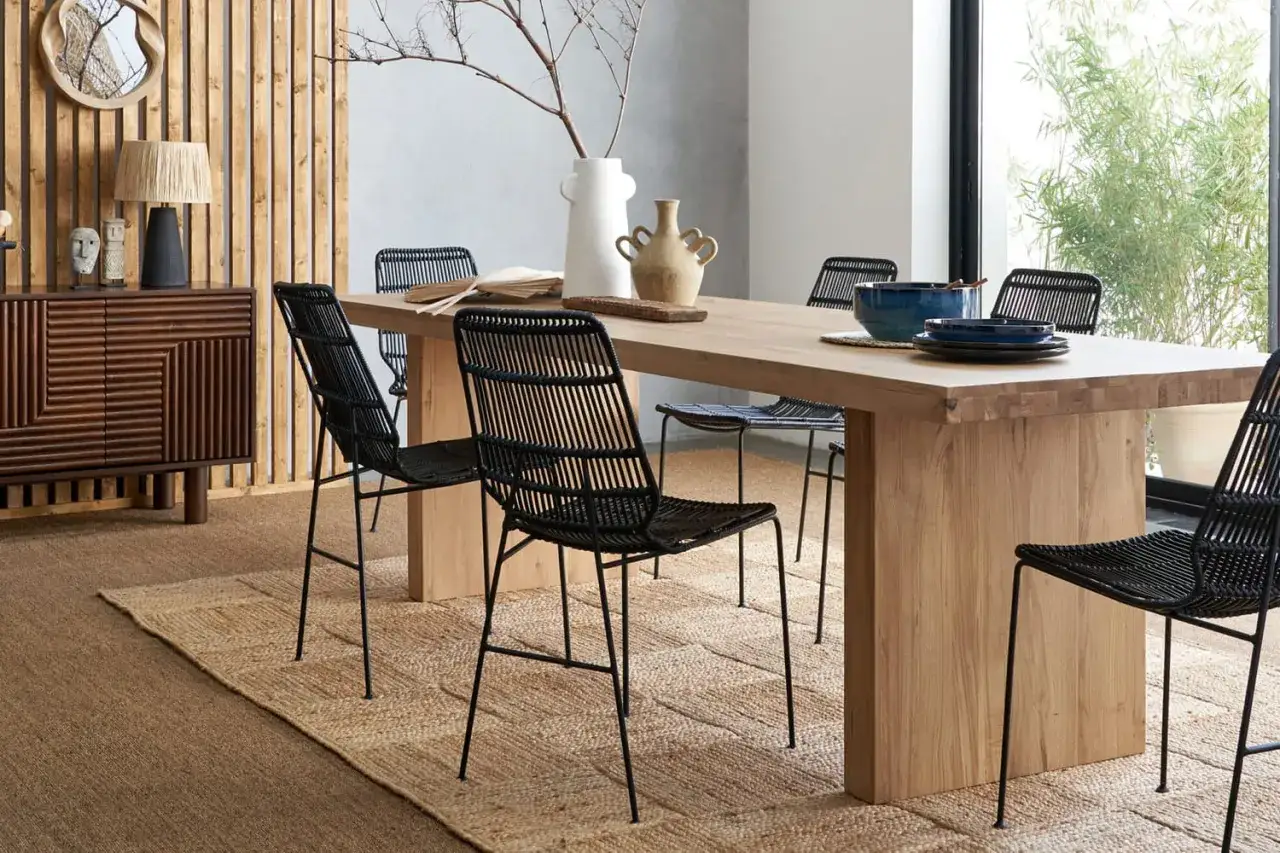 Salle à manger moderne avec table en bois clair et chaises noires. Le mélange bois clair et bois foncé du buffet crée un contraste chaleureux.
