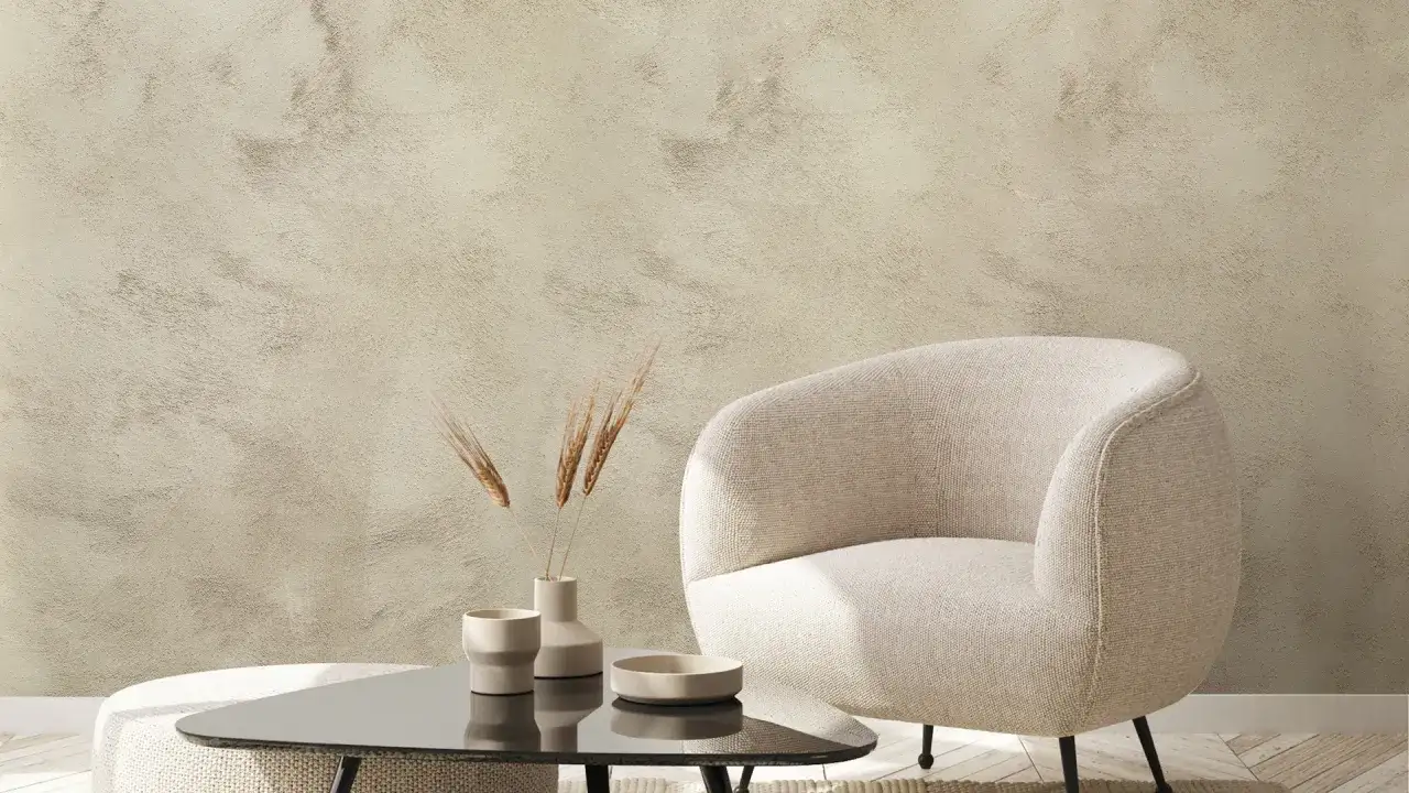 Un fauteuil cosy devant un mur texturé, une peinture à la spatule sur mur aux tons sable. Des épis de blé dans des vases minimalistes sur une table basse.