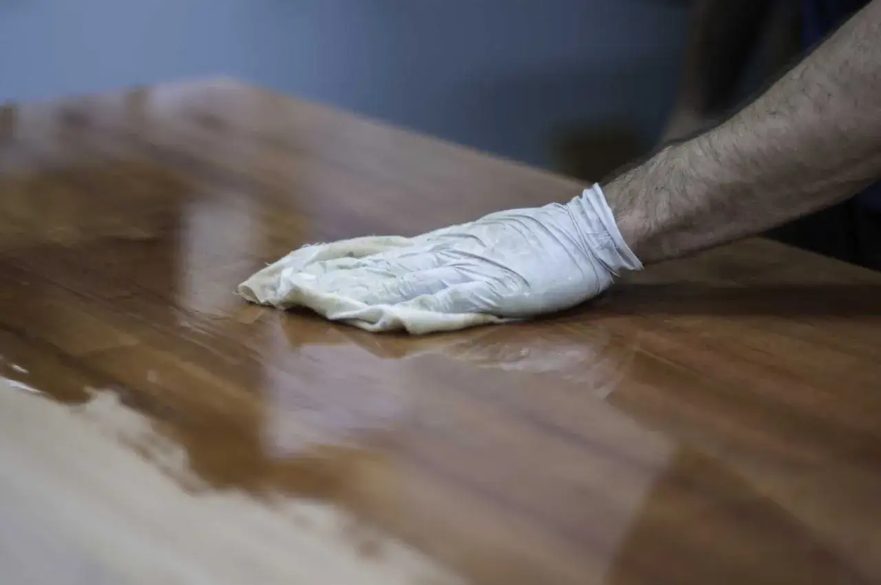 Main d'artisan, gant&eacute;e, applique une couche de vernis sur un meuble en bois pour le polir et le prot&eacute;ger.