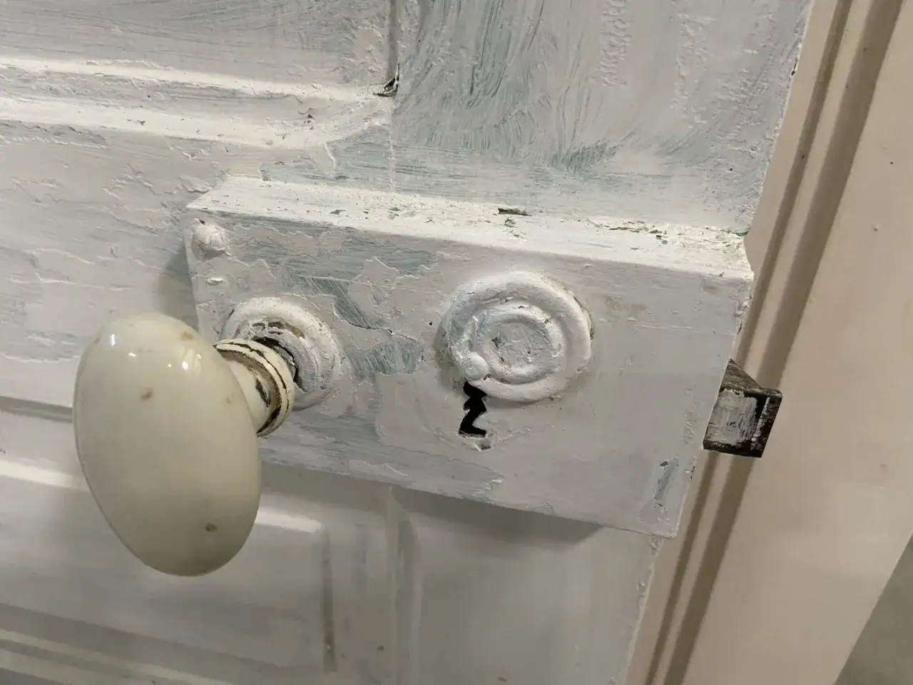 Poignée de porte ancienne recouverte de peinture blanche écaillée, prête à être nettoyée.