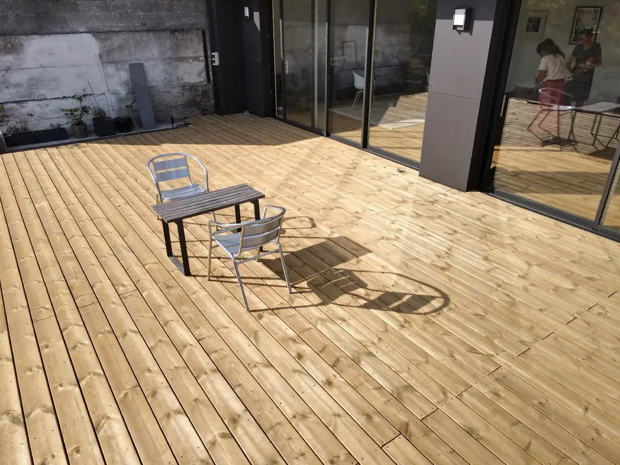 Terrasse en bois clair, trait&eacute;e autoclave pour une durabilit&eacute; accrue. Une table et deux chaises invitent &agrave; la d&eacute;tente.