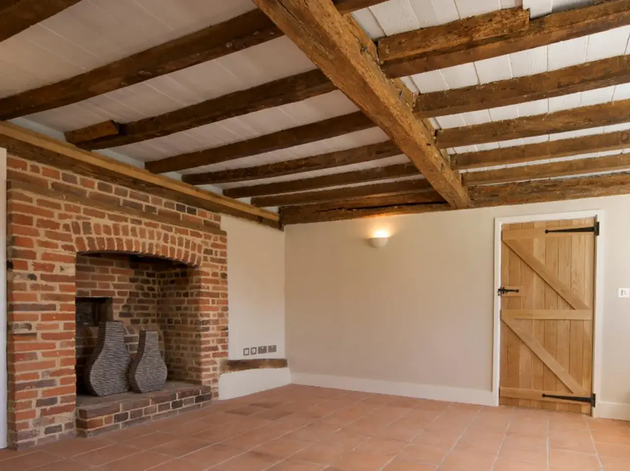 Intérieur rustique avec cheminée en briques, sol en terre cuite et poutres apparentes. Le traitement des poutres anciennes met en valeur le caractère authentique de la pièce.