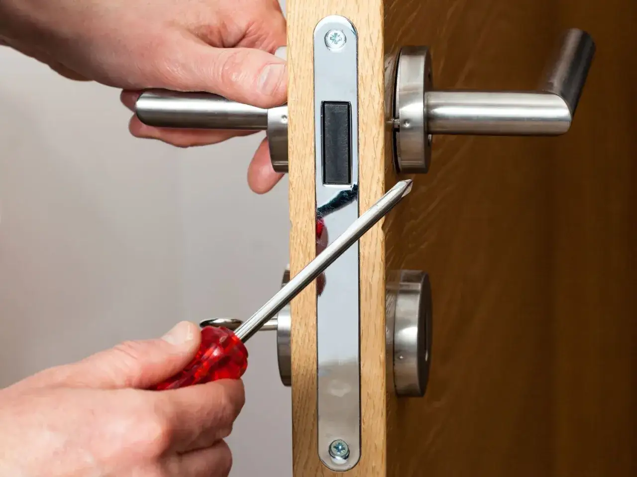 Installation serrure porte : mains ajustant un mécanisme de serrure avec un tournevis sur une porte en bois.