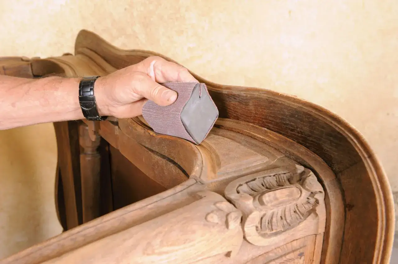 Main d'artisan pon&ccedil;ant d&eacute;licatement les moulures d'un meuble ancien pour lui redonner son &eacute;clat.