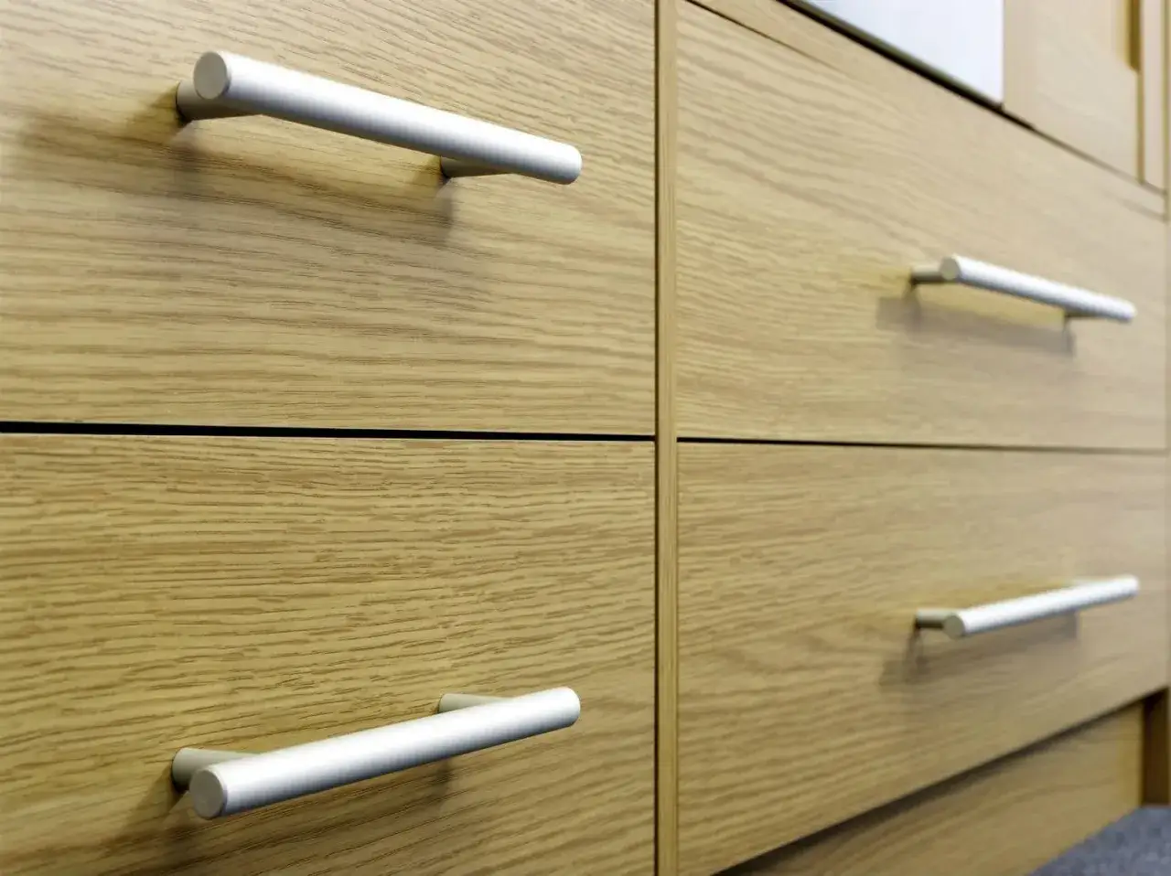 Poign&eacute;es de tiroirs en aluminium sur des meubles en bois clair. Un guide pour comment fixer un bouton de meuble.