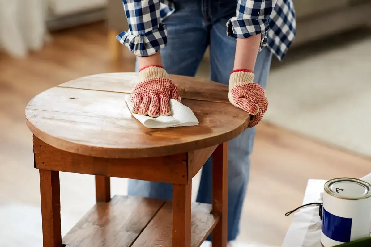 Personne portant des gants rouges et blancs nettoie une table en bois avec un chiffon blanc. Apprenez comment nettoyer une table en bois.