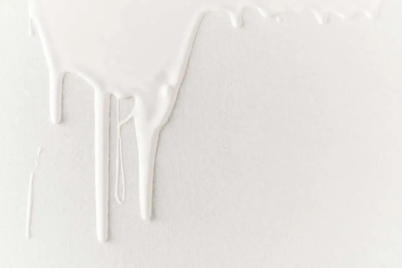 Gouttelettes de peinture blanche tombant sur un mur texturé. Tentative d'enlever gouttelette mur.