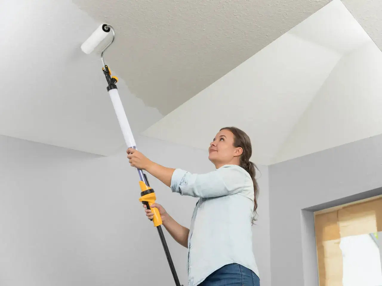 Une femme utilise un rouleau à peinture pour plafond, facilitant la tâche de la peinture à l'huile pour mur et plafond.