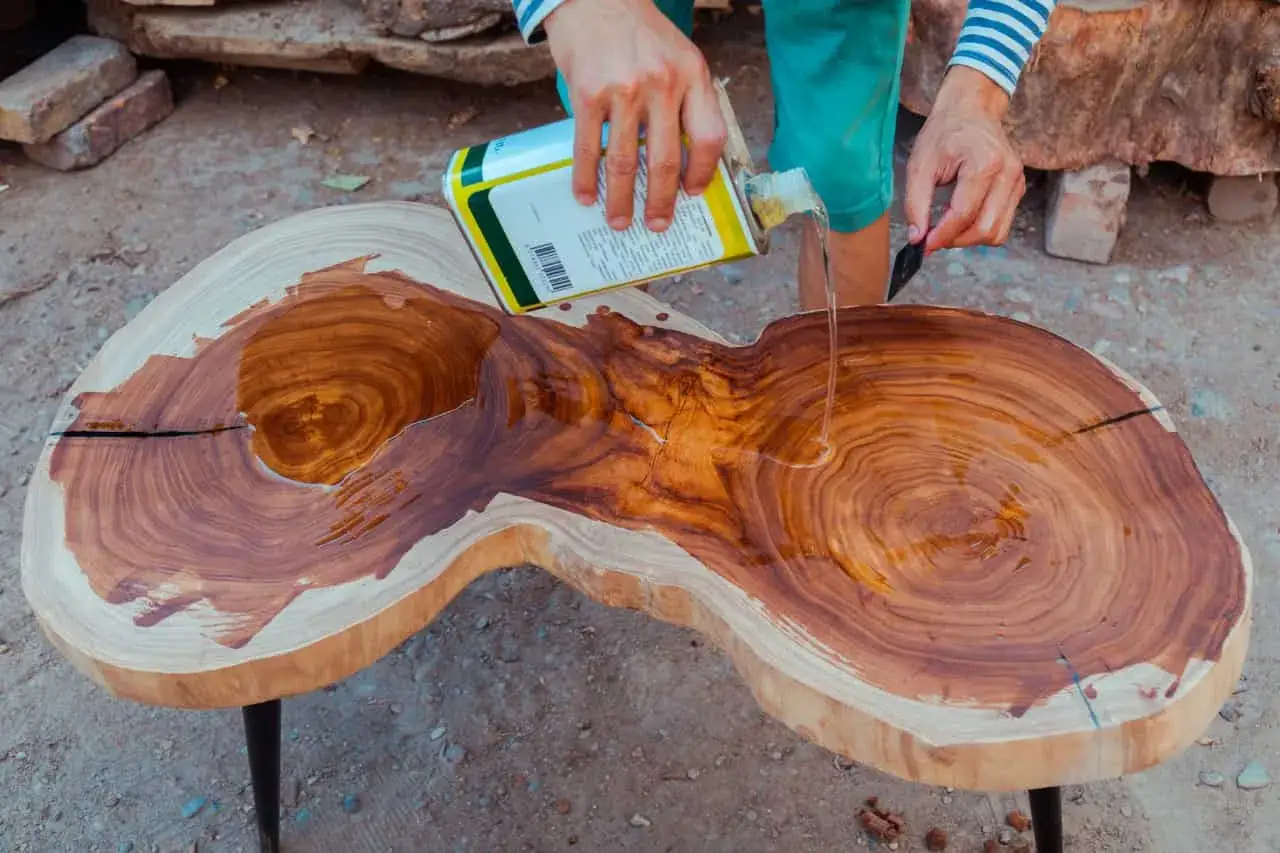 Application d'huile de lin sur un plateau de table en bois brut pour en enlever l'exc&egrave;s et nourrir le bois.