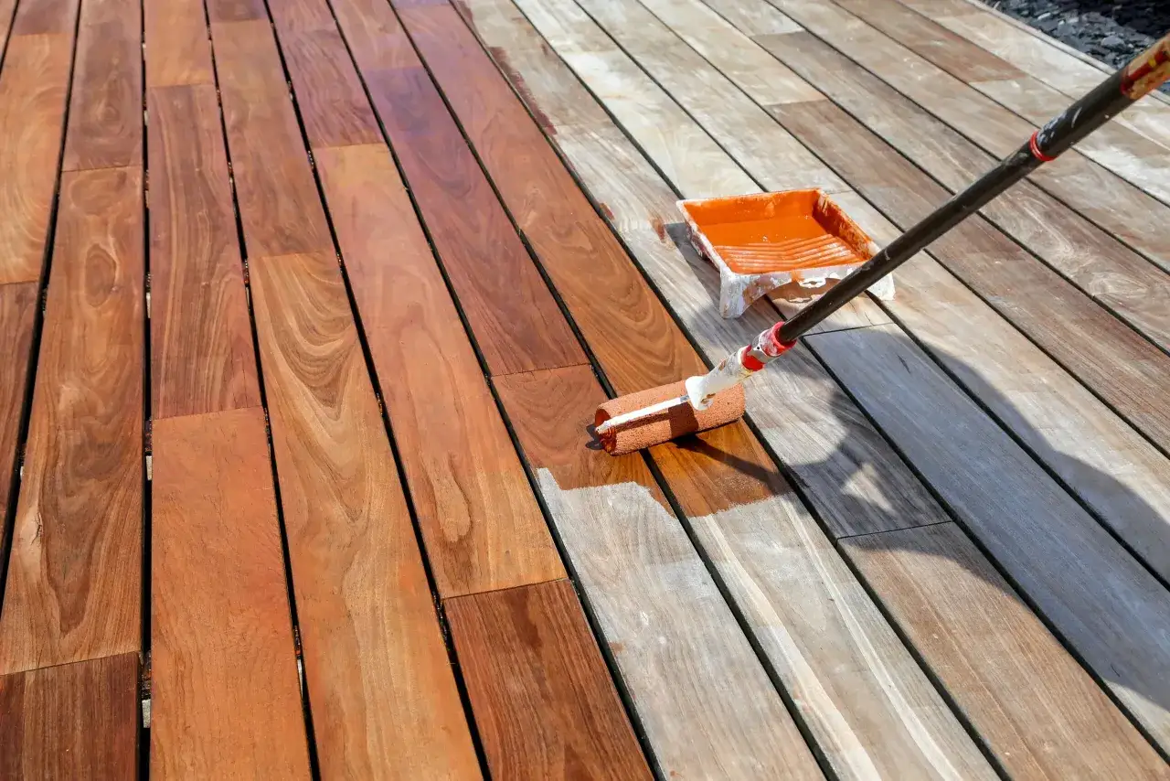 Application d'un saturateur bois intérieur sur une terrasse en bois. Le rouleau dépose le produit, transformant le bois grisâtre en une teinte chaude et protectrice.