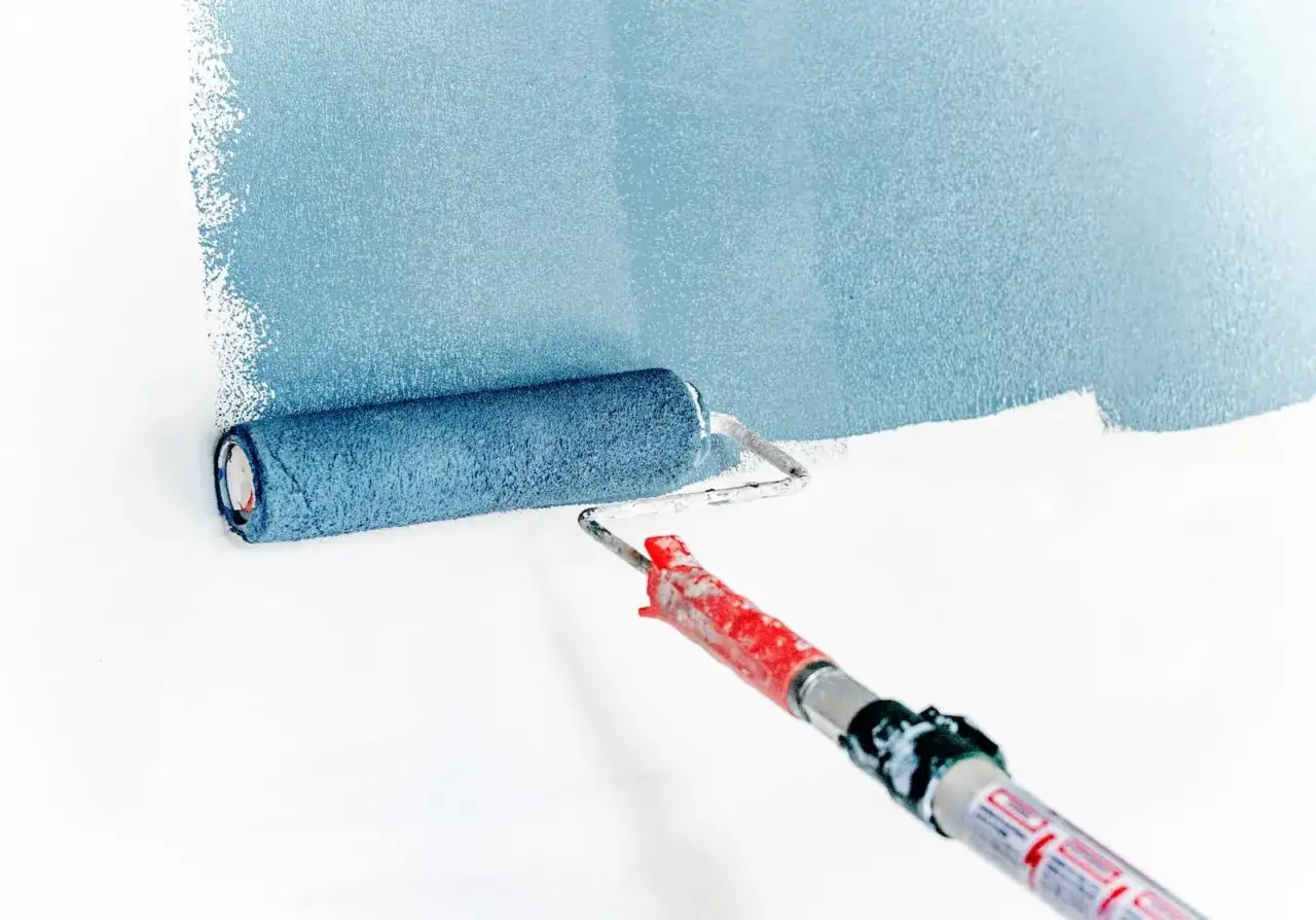 Rouleau appliquant une peinture bleue sur un mur blanc. La technique de peinture murale est visible dans le mouvement du rouleau.