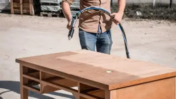 Un homme utilise un appareil pour le décapage chimique bois d'un bureau. La moitié de la surface est déjà propre.