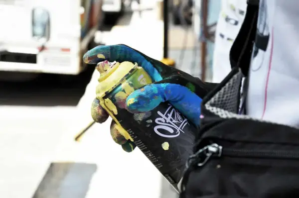 Main tenant une bombe de peinture jaune, un gant coloré montre comment enlever de la bombe de peinture.